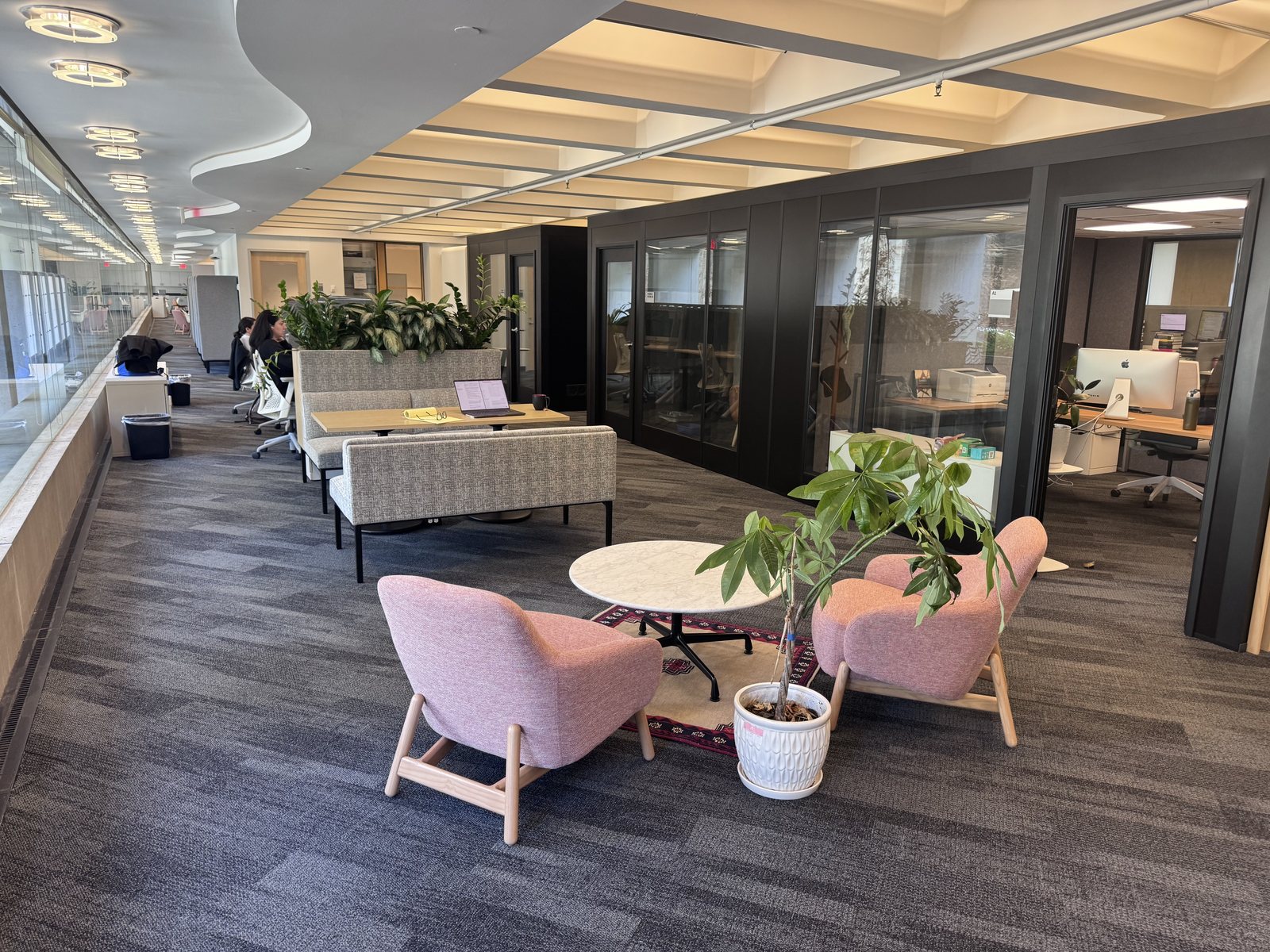 The MAGICS Lab space at Northeastern — open workstations along a window-lined corridor, a soft lounge area with armchairs and plants, and private offices behind glass walls.